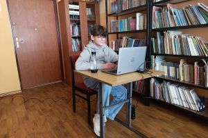 Uczeń siedzący w bibliotece przy laptopie, rozwiązuje Konkurs wiedzy o zdrowym stylu życia Trzymaj Formę.